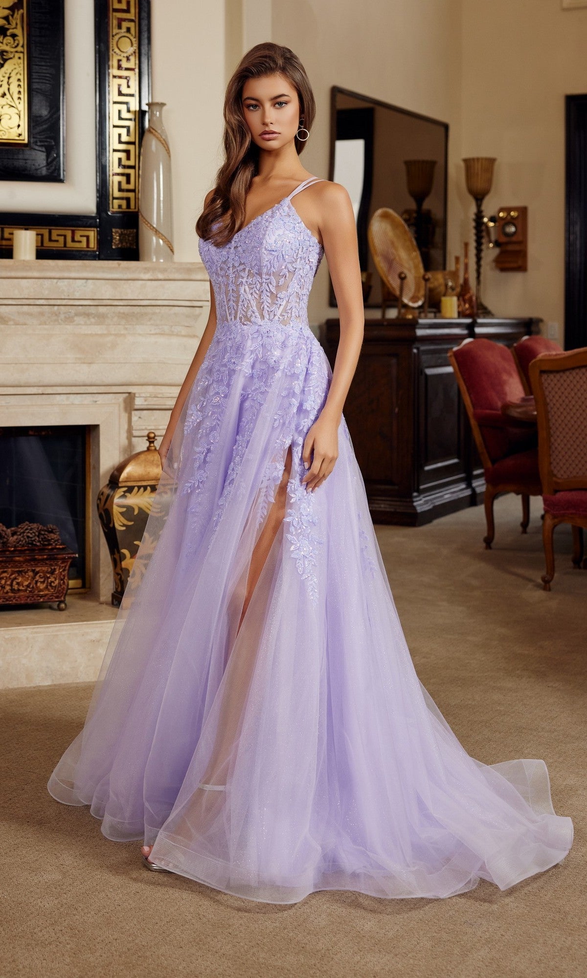 A woman in the Nox Anabel H1882 Long Prom Dress, a lilac tulle gown with lace corset details and a thigh-high slit, stands in an elegant, classic living room.